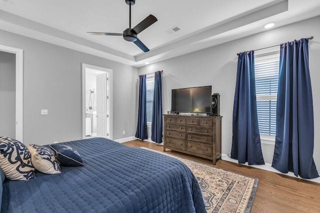 bedroom with ceiling fan, wood finished floors, visible vents, baseboards, and a tray ceiling