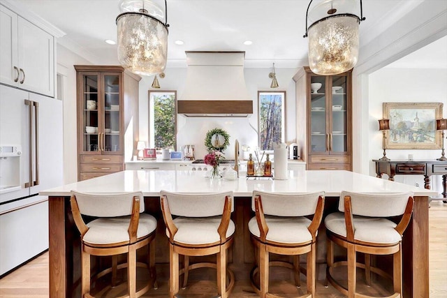 kitchen featuring white appliances, a spacious island, light countertops, glass insert cabinets, and custom range hood