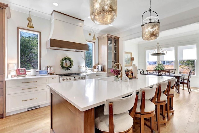 kitchen featuring a spacious island, premium range hood, glass insert cabinets, and light countertops