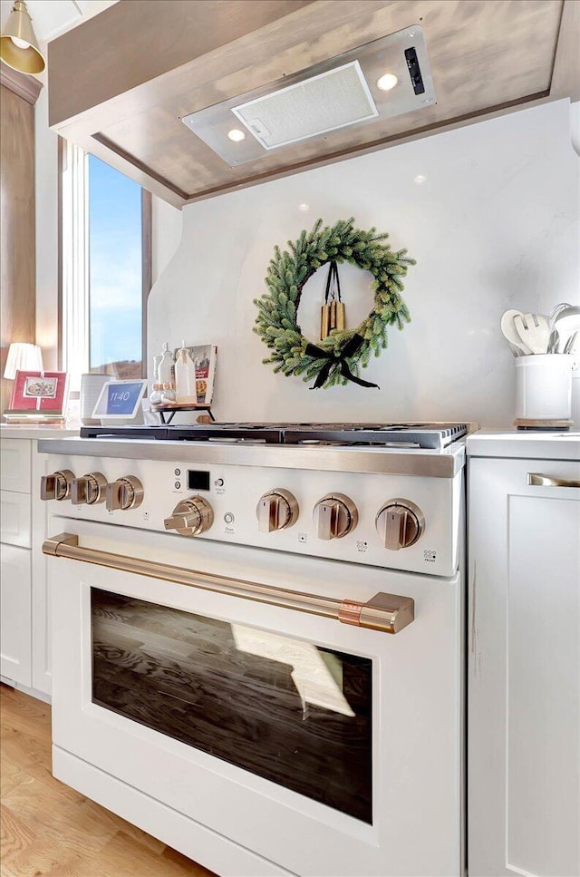 kitchen with light wood-type flooring, high end range oven, and exhaust hood