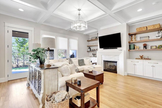 living room featuring a high end fireplace, coffered ceiling, a notable chandelier, and light wood finished floors