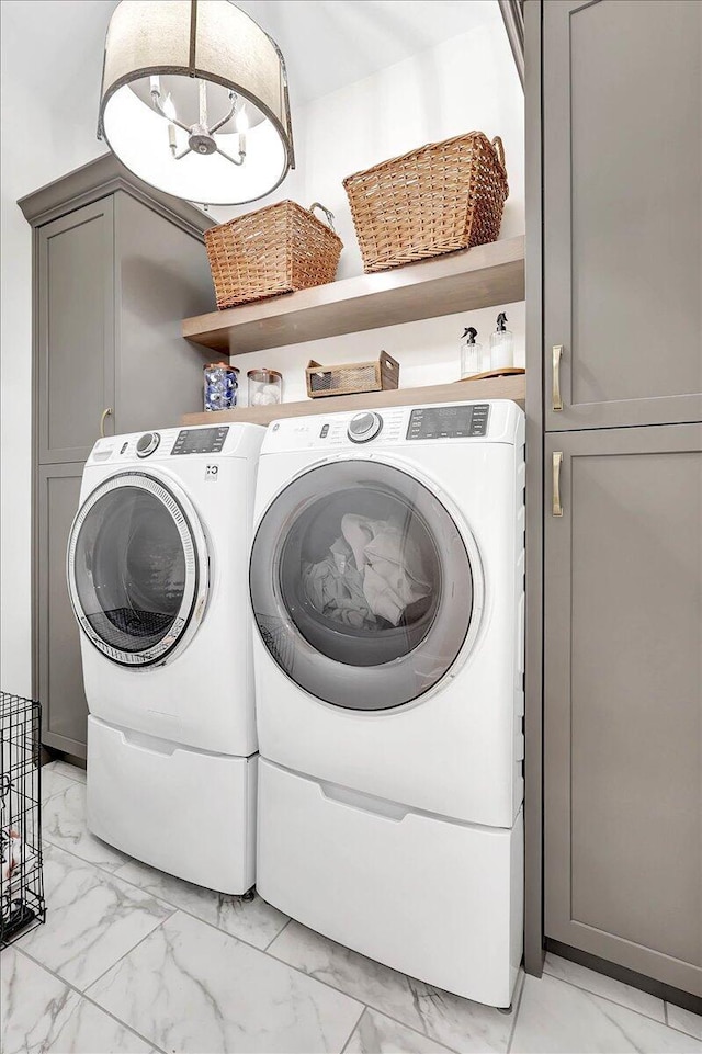 laundry area with marble finish floor, washing machine and dryer, cabinet space, and an inviting chandelier