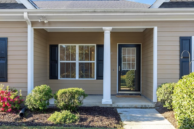 view of exterior entry with covered porch and a shingled roof