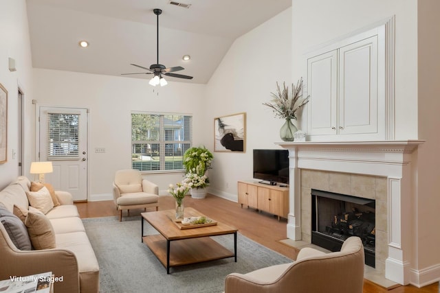 living room with light wood finished floors, lofted ceiling, visible vents, a tile fireplace, and baseboards