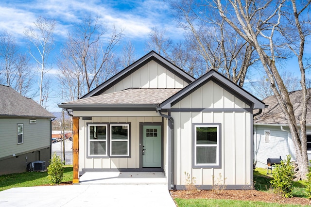 view of front facade with a porch, cooling unit, board and batten siding, and a shingled roof