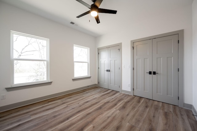 unfurnished bedroom featuring visible vents, baseboards, two closets, and wood finished floors