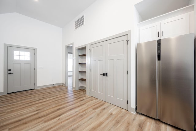 foyer featuring baseboards, light wood-style floors, visible vents, and high vaulted ceiling