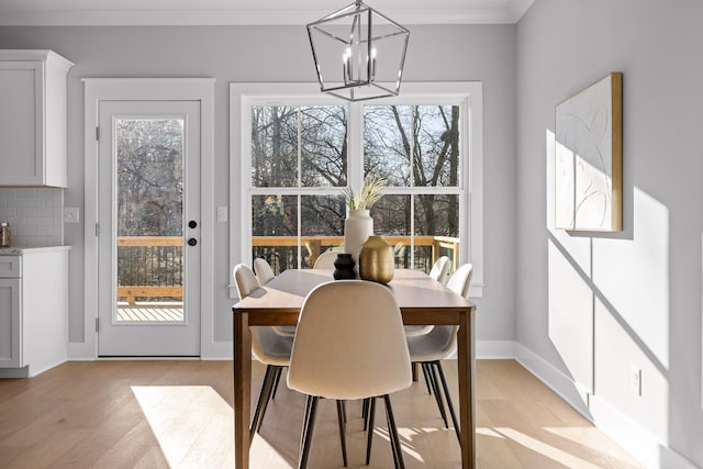 dining area featuring ornamental molding, light wood-type flooring, a notable chandelier, and baseboards