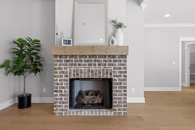 details featuring recessed lighting, wood finished floors, baseboards, ornamental molding, and a brick fireplace