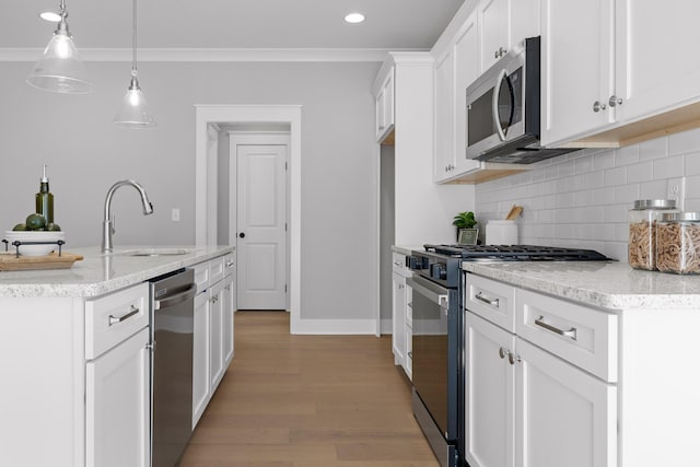 kitchen with appliances with stainless steel finishes, ornamental molding, hanging light fixtures, white cabinetry, and a sink