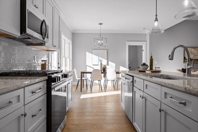 kitchen featuring stainless steel appliances, pendant lighting, a sink, and light stone counters