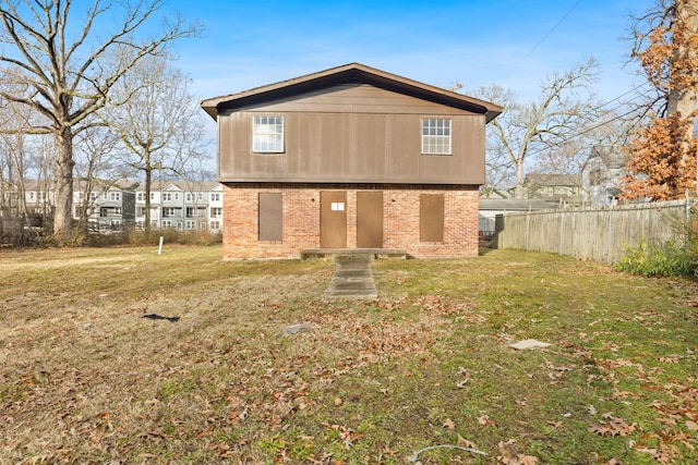 rear view of house featuring brick siding, a lawn, and fence