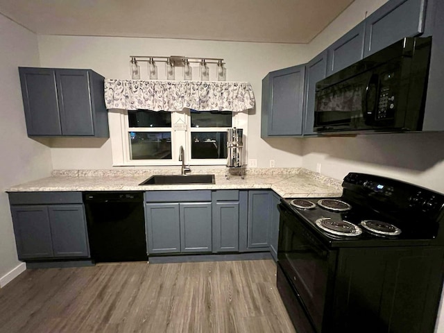 kitchen with light countertops, gray cabinetry, light wood-style floors, a sink, and black appliances