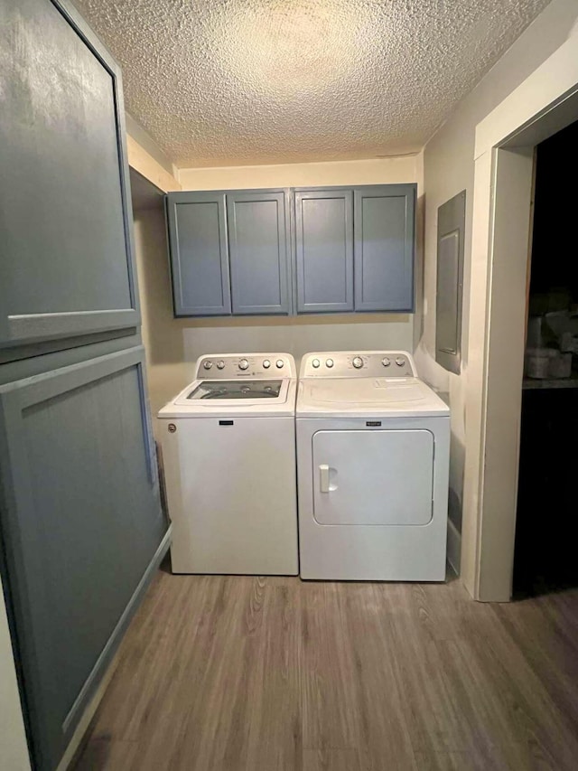 washroom with cabinet space, a textured ceiling, separate washer and dryer, wood finished floors, and electric panel