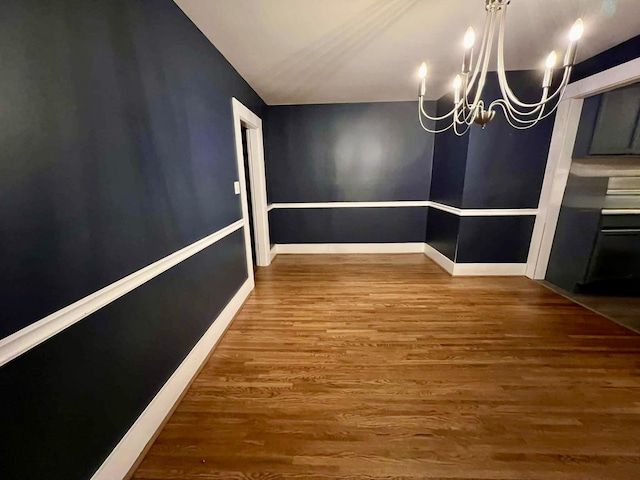 unfurnished dining area featuring baseboards, a chandelier, and wood finished floors