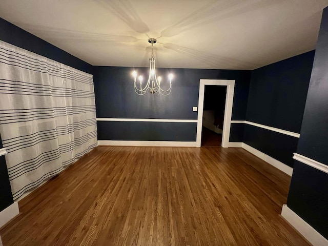 unfurnished dining area featuring a notable chandelier, baseboards, and wood finished floors