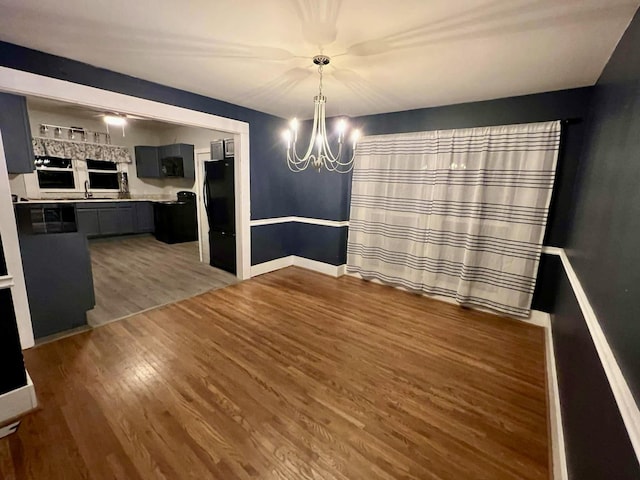 unfurnished dining area with a chandelier, a sink, baseboards, and wood finished floors