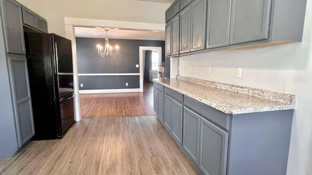 kitchen with light wood-style flooring, freestanding refrigerator, light countertops, gray cabinetry, and a notable chandelier