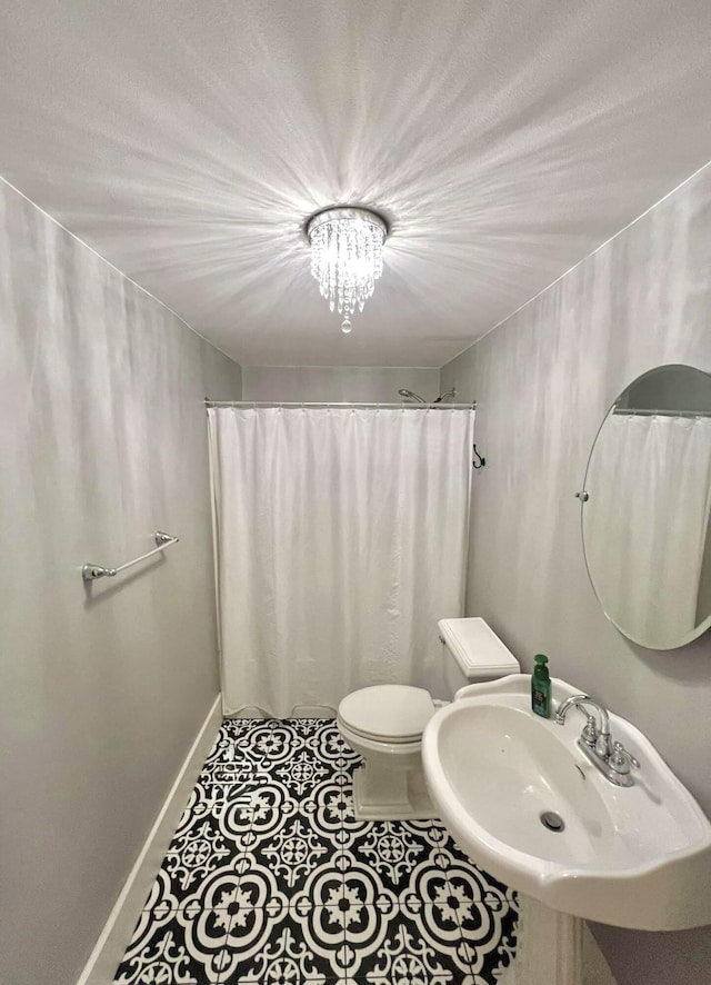 bathroom with baseboards, toilet, a sink, tile patterned flooring, and a notable chandelier