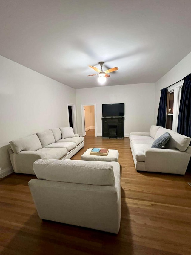 living area with a fireplace, wood finished floors, a ceiling fan, and baseboards