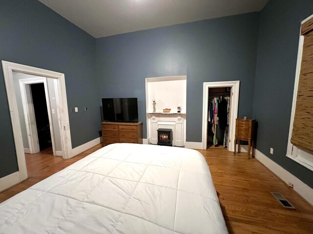 bedroom with wood finished floors, visible vents, baseboards, a lit fireplace, and a walk in closet