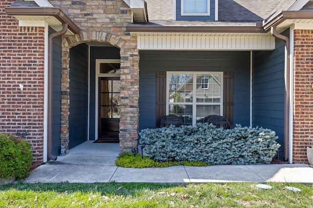 entrance to property with brick siding, a porch, and a shingled roof