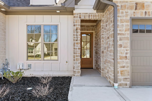 doorway to property with a garage, stone siding, a shingled roof, and board and batten siding