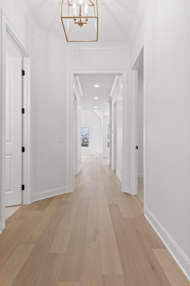 hall with light wood-style floors, baseboards, and crown molding