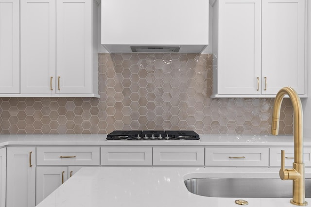 kitchen featuring wall chimney range hood, stainless steel gas cooktop, white cabinets, and a sink