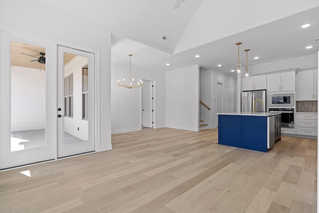 kitchen with decorative light fixtures, stainless steel appliances, light countertops, white cabinetry, and an island with sink