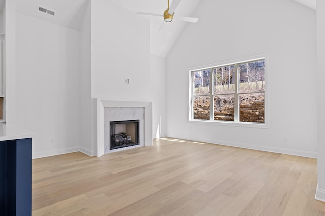 unfurnished living room with visible vents, a premium fireplace, light wood-style floors, ceiling fan, and high vaulted ceiling