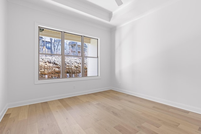 spare room featuring a tray ceiling, light wood finished floors, a ceiling fan, and baseboards