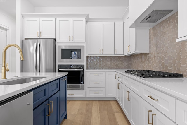 kitchen with stainless steel appliances, light countertops, custom range hood, white cabinetry, and a sink