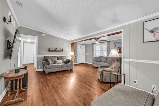 living room with a textured ceiling, wood finished floors, visible vents, and crown molding