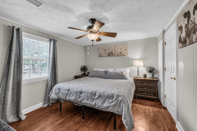 bedroom featuring dark wood-style floors, crown molding, visible vents, ceiling fan, and a textured ceiling