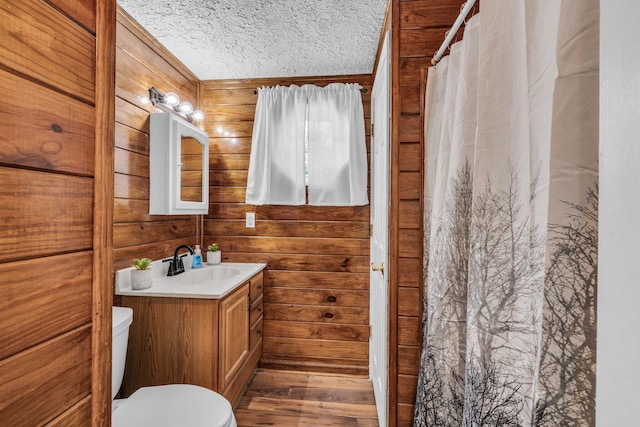 full bathroom featuring toilet, wood walls, a textured ceiling, vanity, and wood finished floors