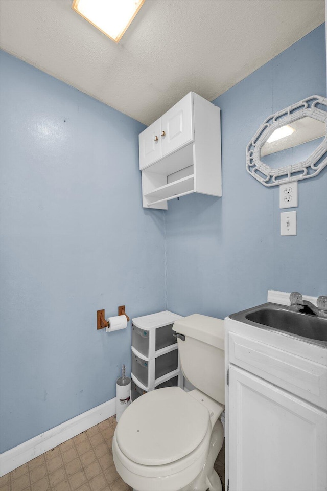 half bathroom with a textured ceiling, toilet, vanity, baseboards, and tile patterned floors