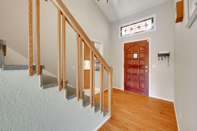 entryway with light wood-type flooring, high vaulted ceiling, baseboards, and stairway