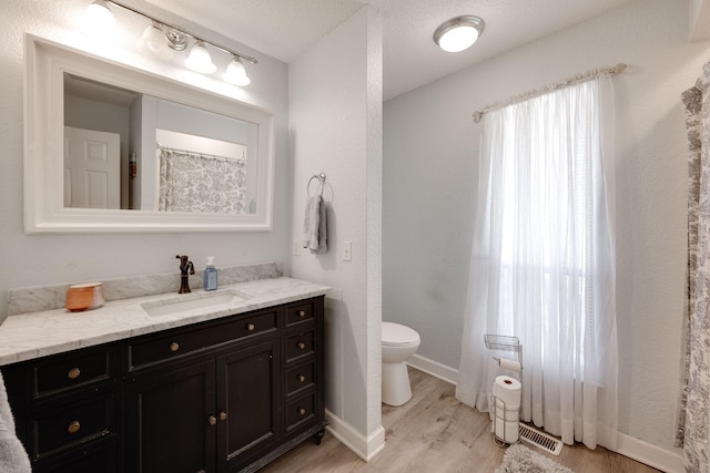 bathroom with visible vents, baseboards, toilet, wood finished floors, and vanity