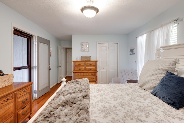 bedroom with light wood-style flooring, a textured ceiling, baseboards, and a closet