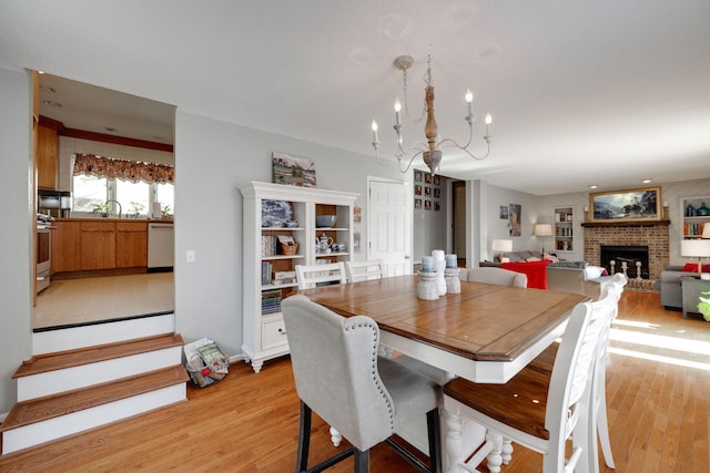 dining space with light wood-style floors, a fireplace, and a notable chandelier