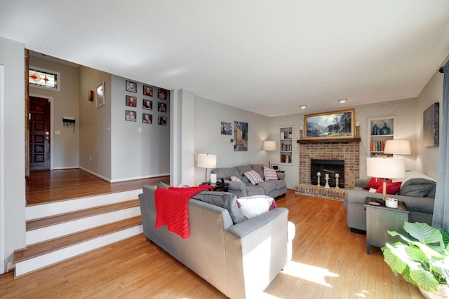 living area featuring light wood-type flooring, a brick fireplace, and baseboards