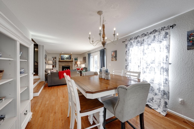 dining area featuring baseboards, a textured wall, light wood-type flooring, a fireplace, and a chandelier