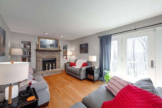 living room featuring a brick fireplace, a textured ceiling, and wood finished floors