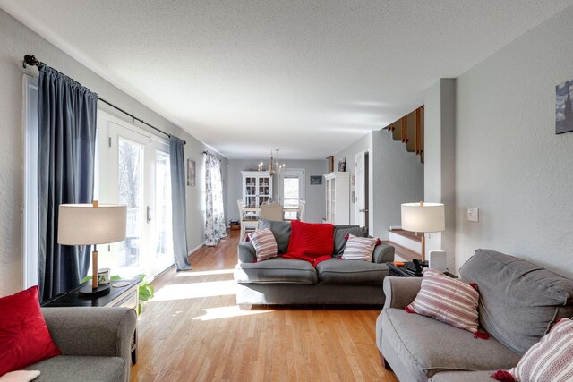 living room with light wood-type flooring, french doors, a notable chandelier, and a textured ceiling