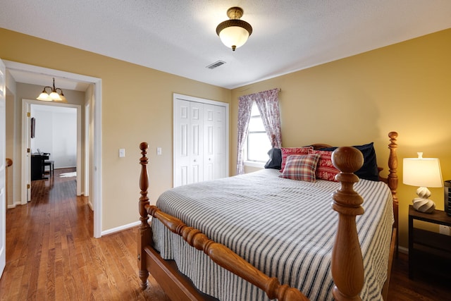 bedroom featuring a closet, visible vents, wood finished floors, a chandelier, and baseboards