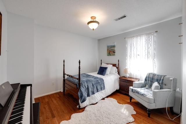 bedroom featuring a textured ceiling, wood finished floors, visible vents, and baseboards