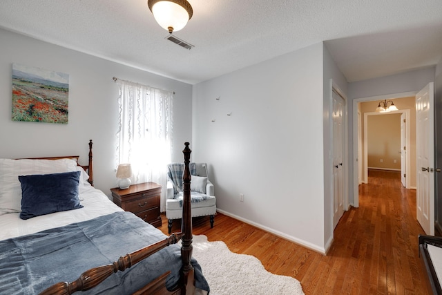 bedroom featuring visible vents, a textured ceiling, baseboards, and wood finished floors