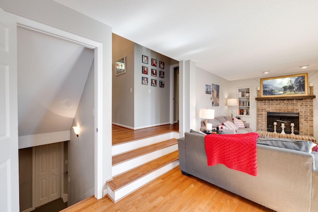 living area with light wood-type flooring, a brick fireplace, built in shelves, and baseboards