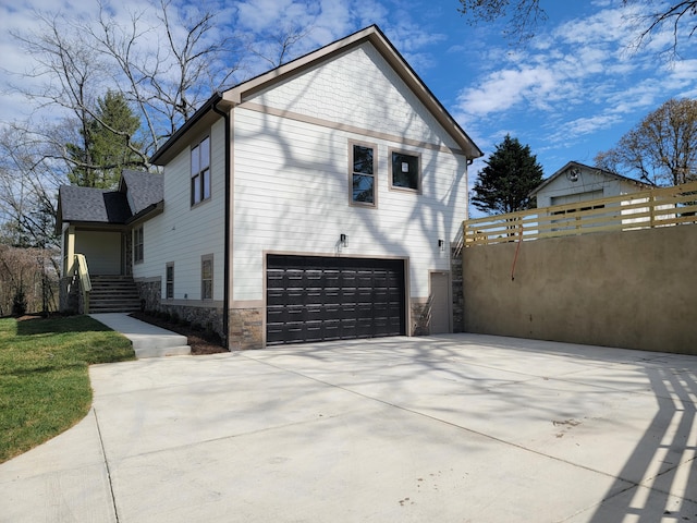 view of home's exterior featuring driveway, stone siding, an attached garage, and fence